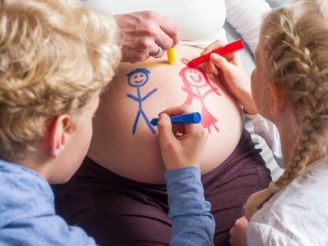 A boy and girl drawing a stick figures on their mom's pregnant belly 